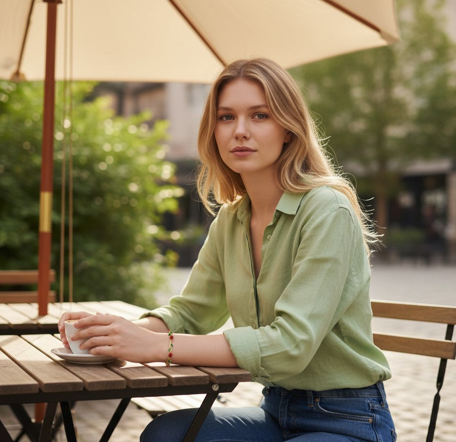 Woman wearing a TITLIYA red and green tulip bracelet while sitting at an outdoor cafe table with a coffee cup.