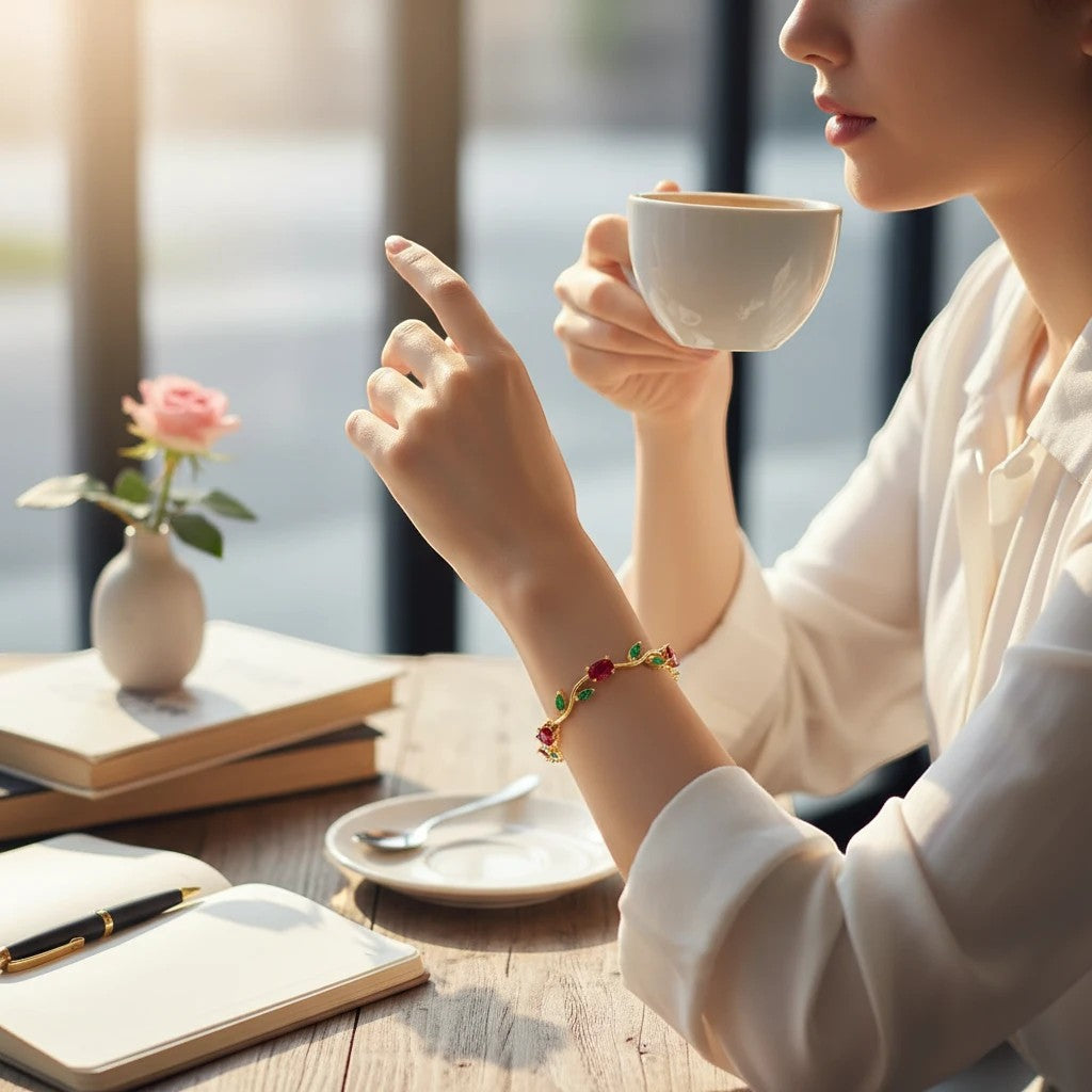TITLIYA gold-tone vine bracelet with red tulip stones and green leaves worn by a woman drinking coffee at a cafe.