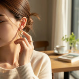 TITLIYA Korean water drop style gold-tone earrings with delicate pearl clusters worn by a woman in a cozy setting.