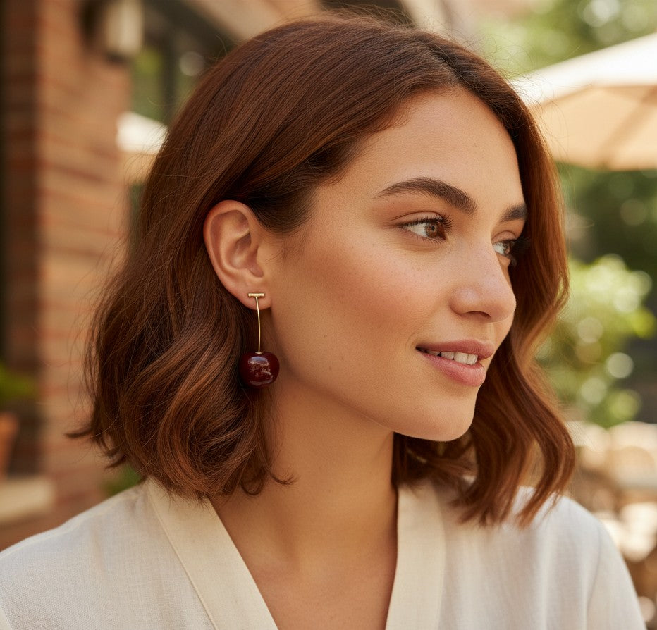 Woman wearing TITLIYA Western cherry drop earrings with a glossy red fruit charm on a gold-tone stem.
