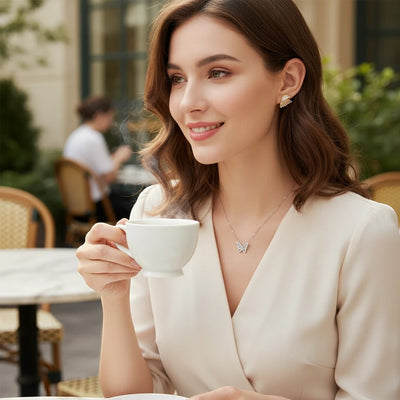 Woman wearing TITLIYA white pearl butterfly stud earrings and matching necklace while drinking coffee at a cafe.